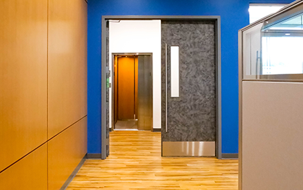 Elvoron LULA elevator entrance in office hallway with glass panels and wood flooring – Garaventa Lift application thumbnail