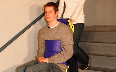 Man with a strange expression in a Powertrac Power evacuation chair operated by a woman