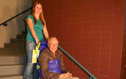 Senior man with glasses in a Powertrac Power evacuation chair operated by a woman