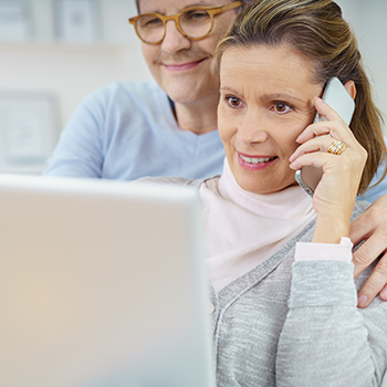 Middle aged couple looks at a computer while the lady speaks on the phone