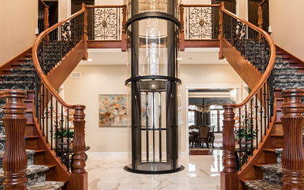 Glass home elevator centered between a grand double staircase in a luxury interior