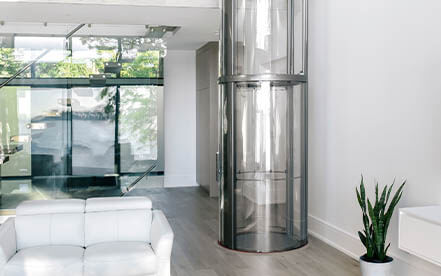 Glass residential elevator installed in a bright living space with modern furnishings