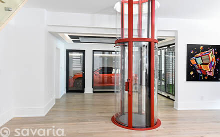 Glass residential elevator installed beside a wooden staircase in a modern home.