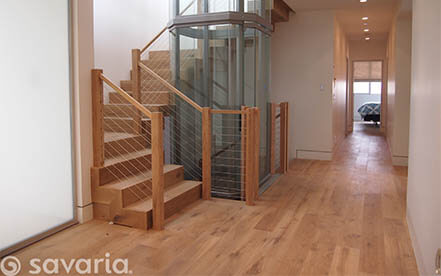 Glass home elevator positioned within a modern curved staircase design