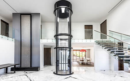 Glass home elevator next to a metal staircase in a contemporary living space
